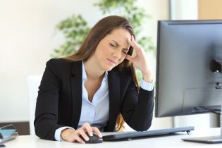 Eine Frau hat Kopfschmerzen wegen schlechter Monitor Ergonomie